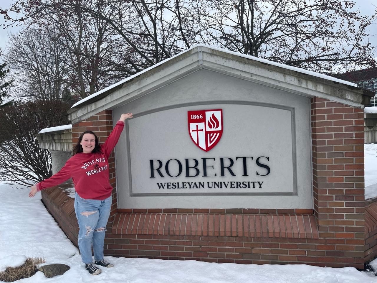 Amber's daughter poses by the Robert Wesleyan University sign.